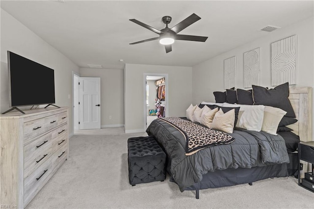 bedroom featuring light colored carpet, a walk in closet, a ceiling fan, baseboards, and visible vents