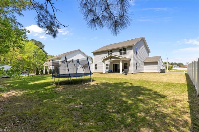 rear view of property with a trampoline and a yard