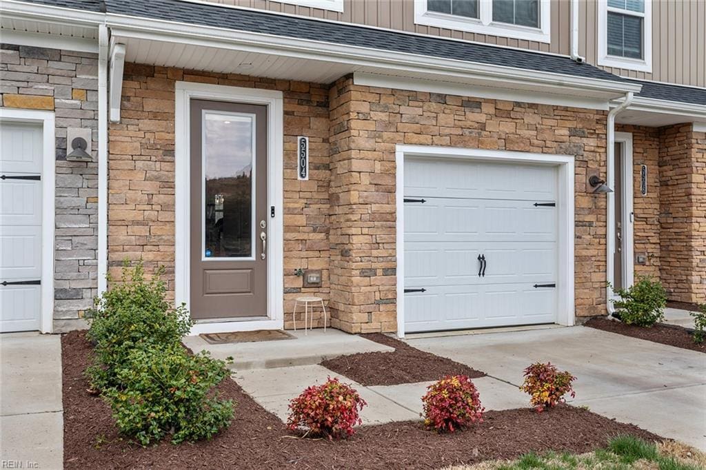 5504 Wenrich Dr, Richmond, VA 23227 - view of exterior entry with board and batten siding, driveway, roof with shingles, and a garage