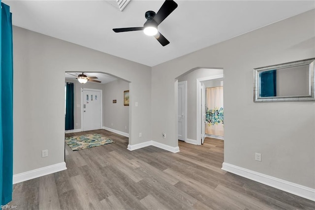 spare room featuring baseboards, arched walkways, ceiling fan, and wood finished floors