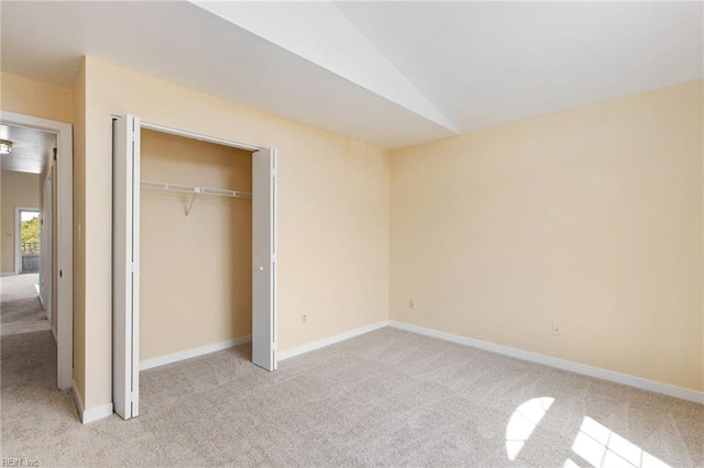 unfurnished bedroom featuring vaulted ceiling, a closet, light carpet, and baseboards