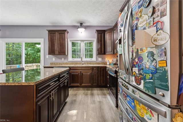kitchen featuring stainless steel appliances, a sink, a textured ceiling, light stone countertops, and light wood-type flooring