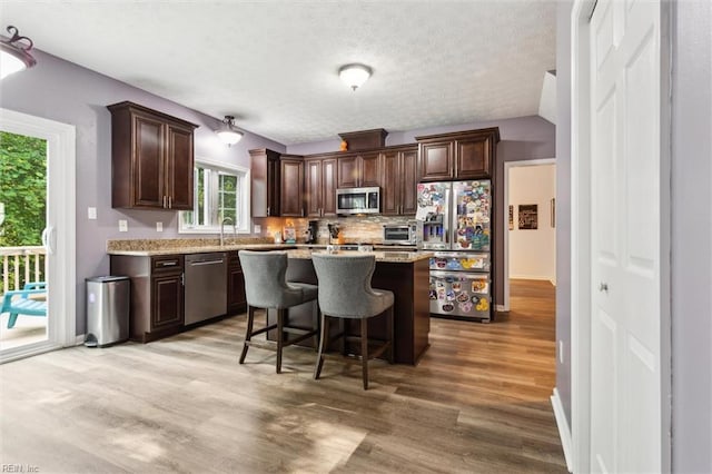 kitchen featuring stainless steel appliances, dark brown cabinetry, light wood-type flooring, a breakfast bar area, and a center island