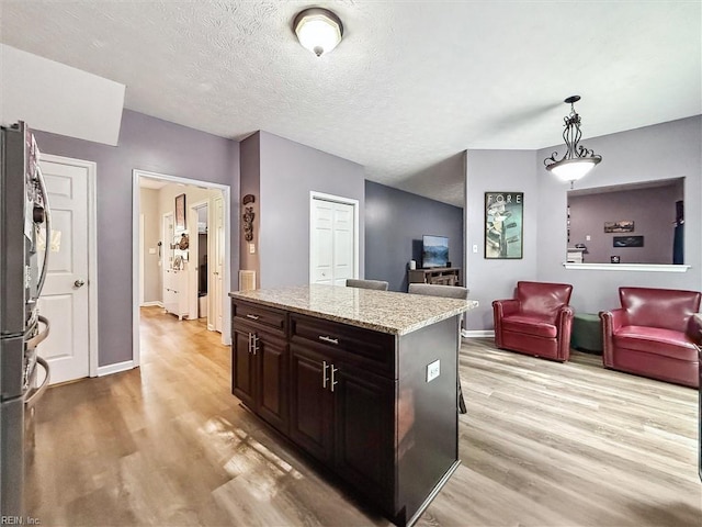 kitchen with light wood-type flooring, baseboards, a center island, light stone counters, and a textured ceiling
