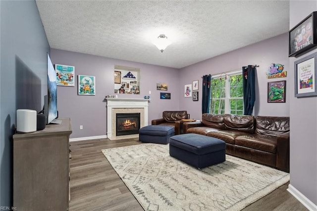 living room with wood finished floors, baseboards, a fireplace with flush hearth, and a textured ceiling