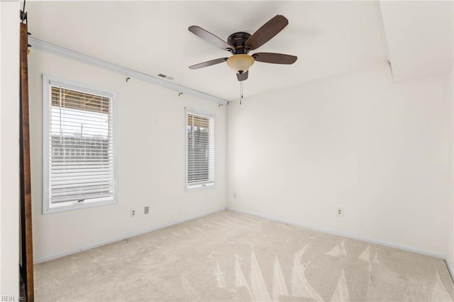 spare room featuring light colored carpet, a ceiling fan, plenty of natural light, and baseboards