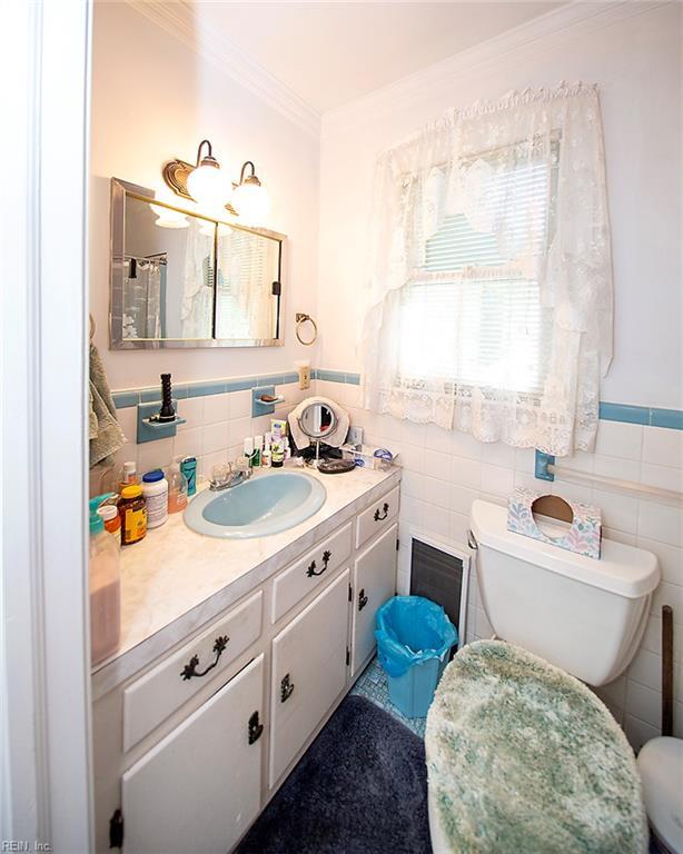 bathroom with toilet, a wainscoted wall, tile walls, vanity, and ornamental molding