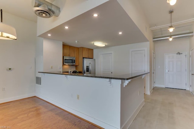 kitchen featuring baseboards, appliances with stainless steel finishes, a breakfast bar area, and brown cabinets