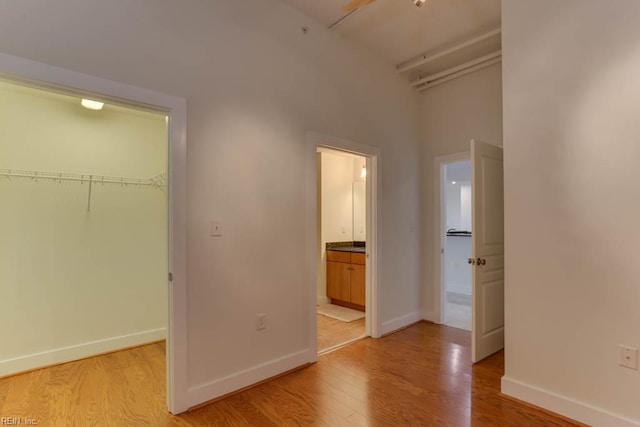 unfurnished bedroom with light wood-type flooring, baseboards, a walk in closet, and a closet