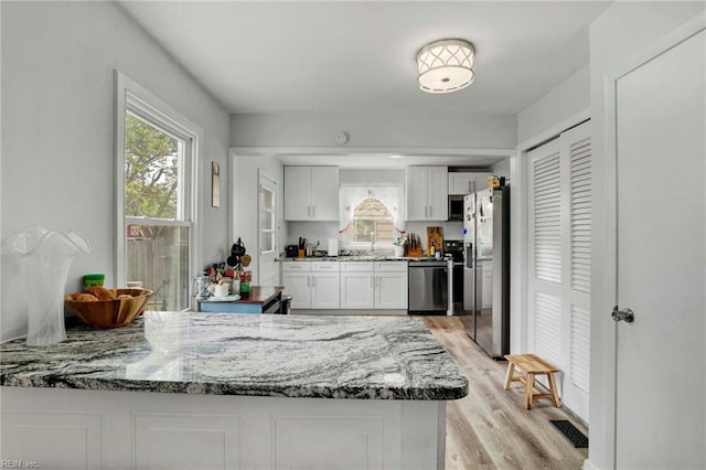 kitchen featuring a healthy amount of sunlight, appliances with stainless steel finishes, light wood-style flooring, and white cabinetry