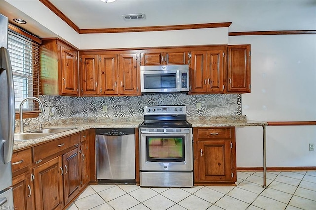 kitchen with brown cabinetry, ornamental molding, a sink, backsplash, and appliances with stainless steel finishes