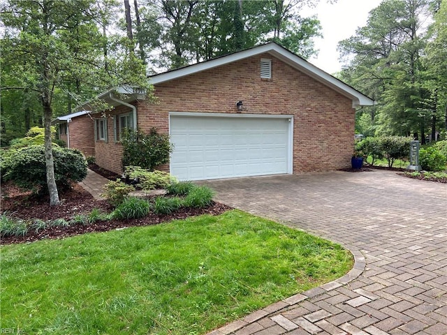 view of side of home with an attached garage, brick siding, decorative driveway, and a lawn