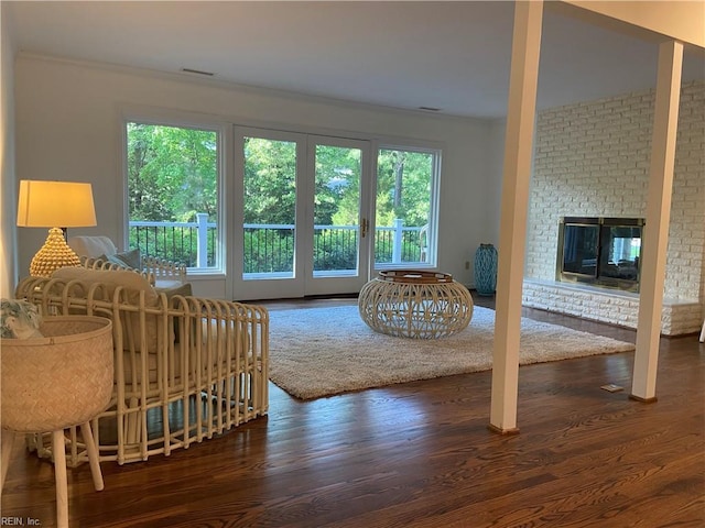 living area featuring a brick fireplace, crown molding, plenty of natural light, and wood finished floors