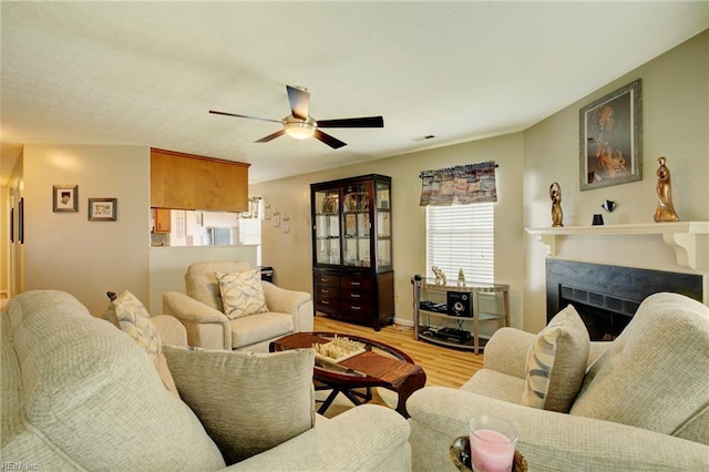 living room featuring a fireplace, a ceiling fan, baseboards, wood finished floors, and visible vents