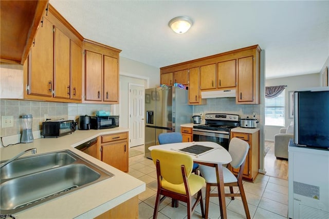 kitchen featuring light tile patterned flooring, under cabinet range hood, tasteful backsplash, a sink, and appliances with stainless steel finishes