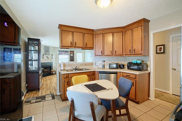 kitchen with brown cabinetry, black microwave, stainless steel dishwasher, a sink, and light countertops