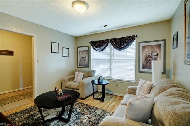 living area featuring a textured ceiling, visible vents, baseboards, and light wood finished floors