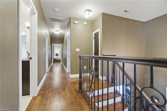 hall featuring wood finished floors, attic access, an upstairs landing, visible vents, and baseboards
