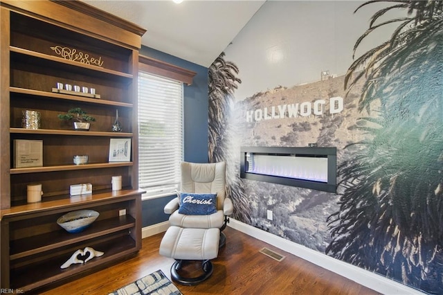 living area featuring wood finished floors, visible vents, a fireplace, vaulted ceiling, and baseboards