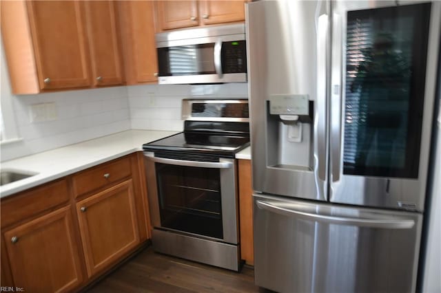 kitchen with tasteful backsplash, brown cabinets, dark wood-type flooring, light countertops, and appliances with stainless steel finishes