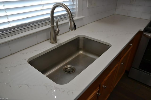 interior details featuring a sink, decorative backsplash, light stone counters, and stainless steel stove