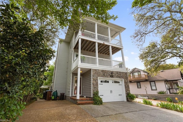view of front facade with concrete driveway, an attached garage, stone siding, and a balcony