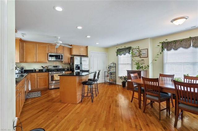 kitchen featuring stainless steel appliances, a breakfast bar, a center island, dark countertops, and light wood-style floors