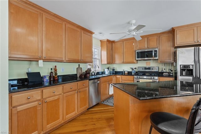 kitchen with light wood-style flooring, a breakfast bar, dark stone counters, ceiling fan, and appliances with stainless steel finishes