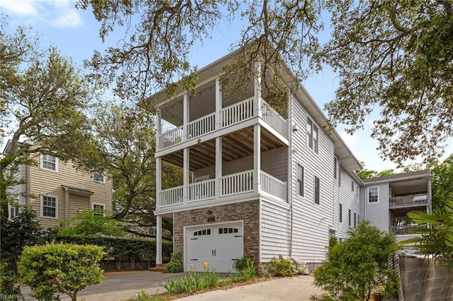 view of home's exterior featuring stone siding, driveway, a garage, and a balcony