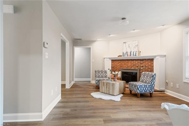 sitting room with a brick fireplace, baseboards, visible vents, and wood finished floors