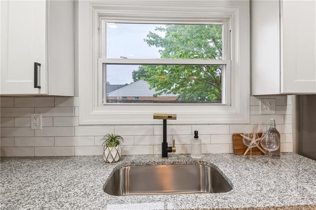 room details with white cabinetry, light stone countertops, tasteful backsplash, and a sink