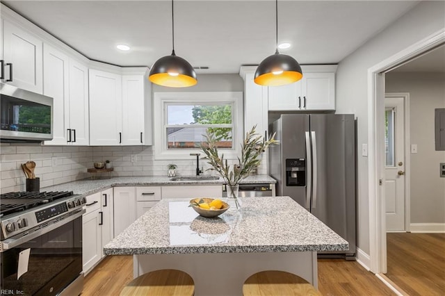 kitchen featuring a sink, stainless steel appliances, light wood finished floors, backsplash, and white cabinets