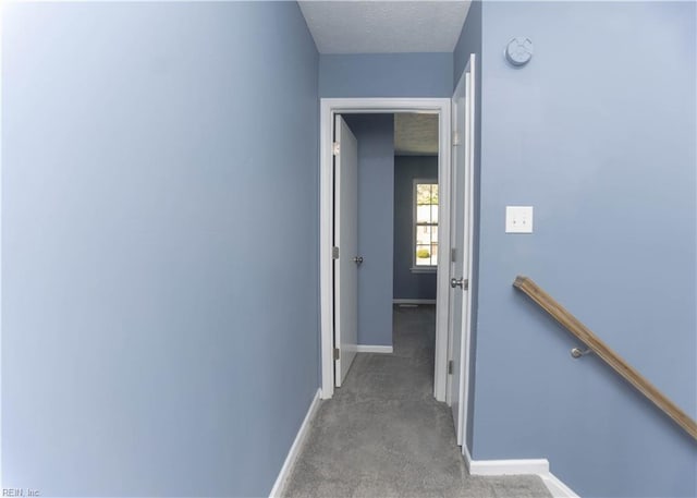 hallway featuring baseboards, a textured ceiling, an upstairs landing, and carpet
