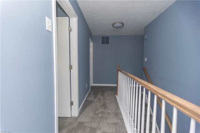 hall featuring a textured ceiling, baseboards, visible vents, an upstairs landing, and carpet floors