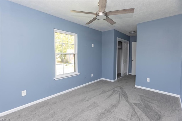 unfurnished bedroom with a textured ceiling, carpet flooring, baseboards, and a ceiling fan