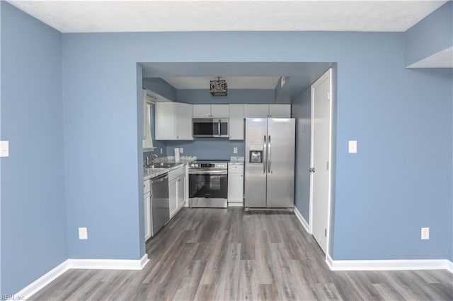 kitchen featuring baseboards, dark wood finished floors, a sink, white cabinets, and appliances with stainless steel finishes
