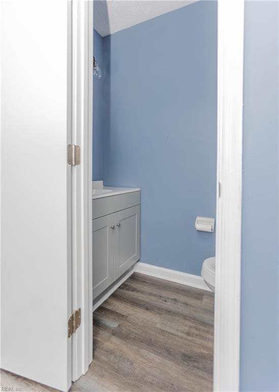 bathroom featuring vanity, wood finished floors, baseboards, and toilet