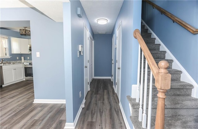 corridor featuring stairs, dark wood-style flooring, and baseboards