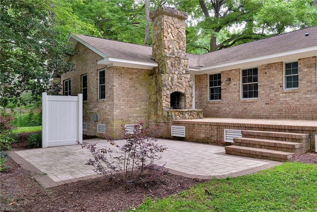 back of house featuring a patio, crawl space, a chimney, brick siding, and roof with shingles