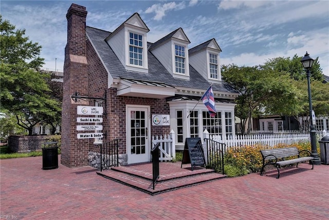 cape cod home with brick siding, fence, and a chimney