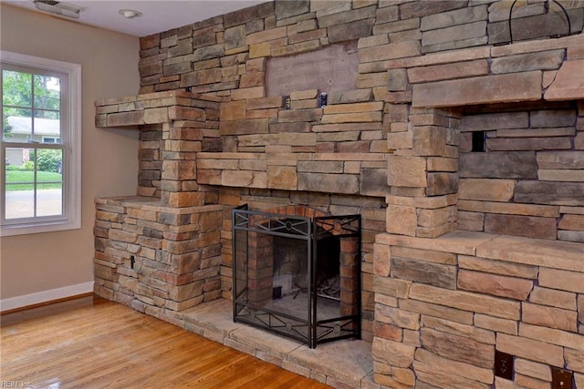room details featuring baseboards, a stone fireplace, visible vents, and wood finished floors