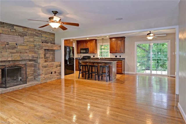 living room with light wood-type flooring, baseboards, a ceiling fan, and a fireplace