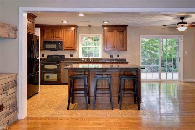 kitchen with a ceiling fan, a sink, brown cabinets, a kitchen breakfast bar, and black appliances