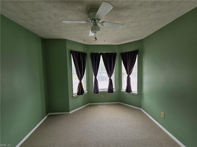 carpeted spare room featuring a textured ceiling, baseboards, a ceiling fan, and visible vents