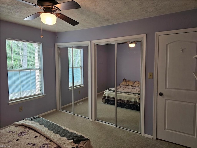 carpeted bedroom featuring multiple windows, two closets, and a textured ceiling