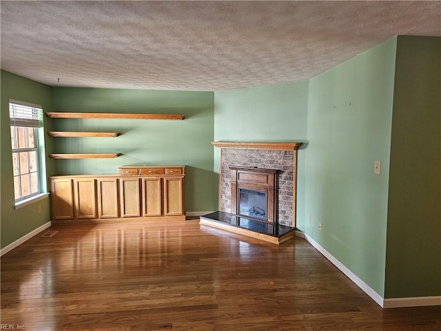 unfurnished living room with baseboards, a fireplace with raised hearth, a textured ceiling, and wood finished floors