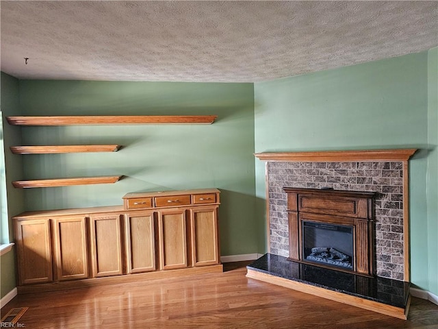 unfurnished living room with a fireplace with raised hearth, a textured ceiling, and wood finished floors