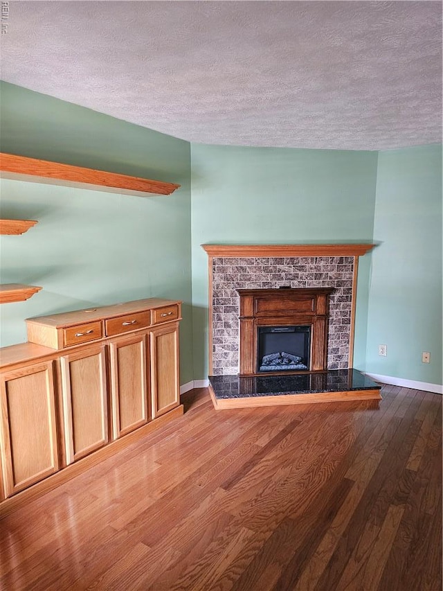 unfurnished living room with a textured ceiling, baseboards, wood finished floors, and a fireplace with raised hearth