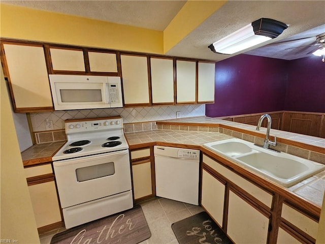 kitchen featuring a textured ceiling, tile counters, a sink, and white appliances
