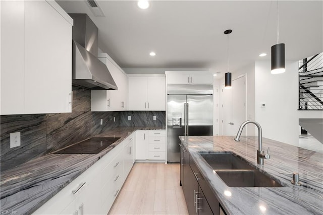 kitchen featuring stainless steel built in refrigerator, a sink, wall chimney range hood, black electric stovetop, and tasteful backsplash